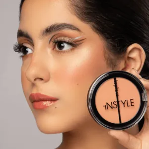 Gros plan d'une femme au maquillage soigné tenant un poudrier Topface Instyle Twin Blush On corail-pêche près de son visage.