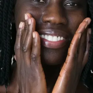 Une femme à la peau noire applique du soin hydratant Evoluderm à la carotte sur son visage radieux en souriant.