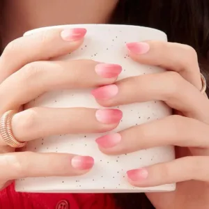Faux ongles autocollants Kiss imPRESS Beat The Heat rose dégradé tenus sur une tasse, manucure tendance sans colle 18+.
