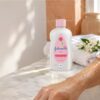 Huile pour le corps appliquée sur un avant-bras encore humide après la douche, flacon transparent et serviette blanche sur une étagère en marbre.